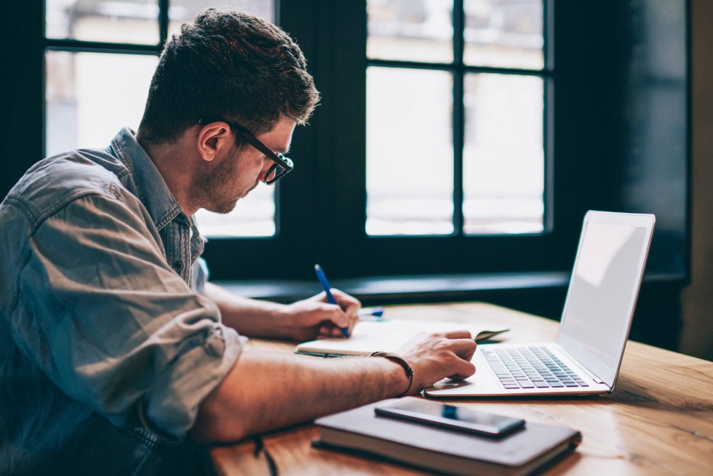 Man on his laptop while writing in his notebook