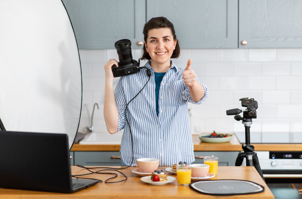 a female photographer holding a camera and making a thumbs up