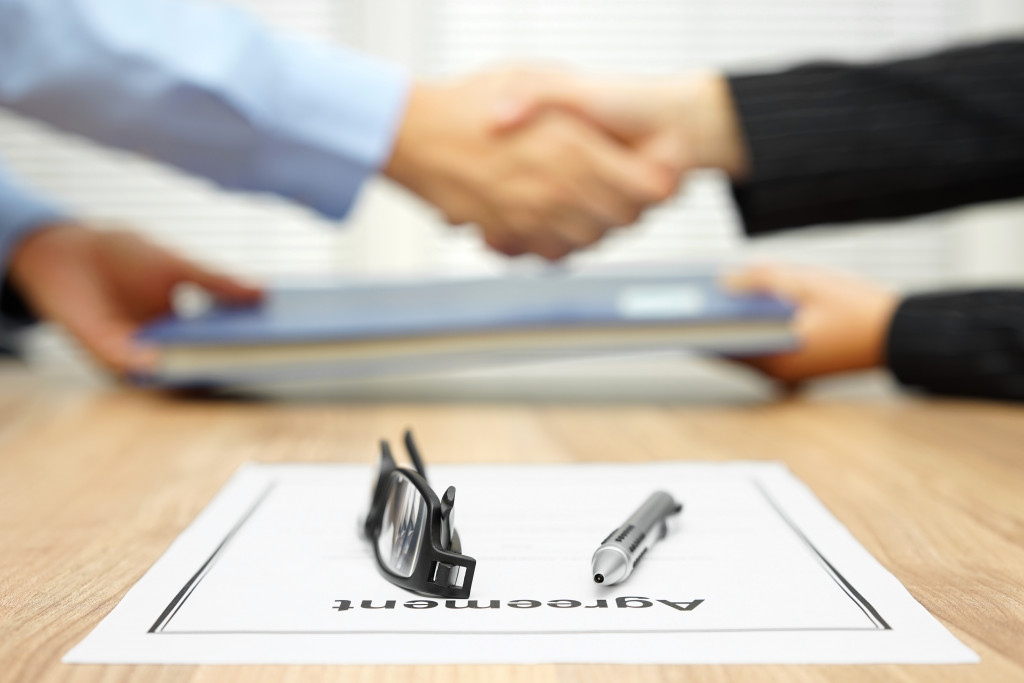 Agreement with a pen and glasses on top with a creditor and shaking hands with a client in the background.